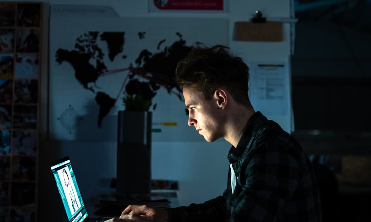 A man working at a laptop in a dimly lit room — focused but stalled